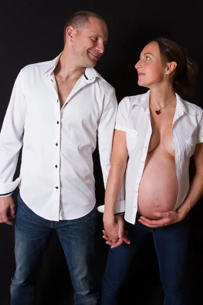 Novos Pais Olhando Juntos Barriga Mãe Grávida Sobre Fundo Preto — Fotografia de Stock