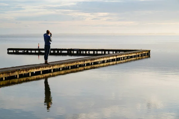 single woman standing on wooden pier pontoon access boat in Biscarrosse lake sunrise