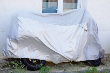 Motosiklet sokağı gümüş kaplı gri motosiklet brandası ceketle korunuyor.