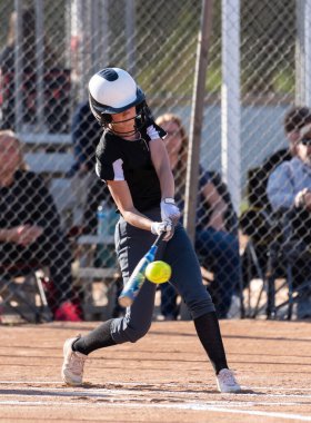 Liseli bayan softball oyuncusu gözünü toptan ayırmazken iyi temas kuruyor..