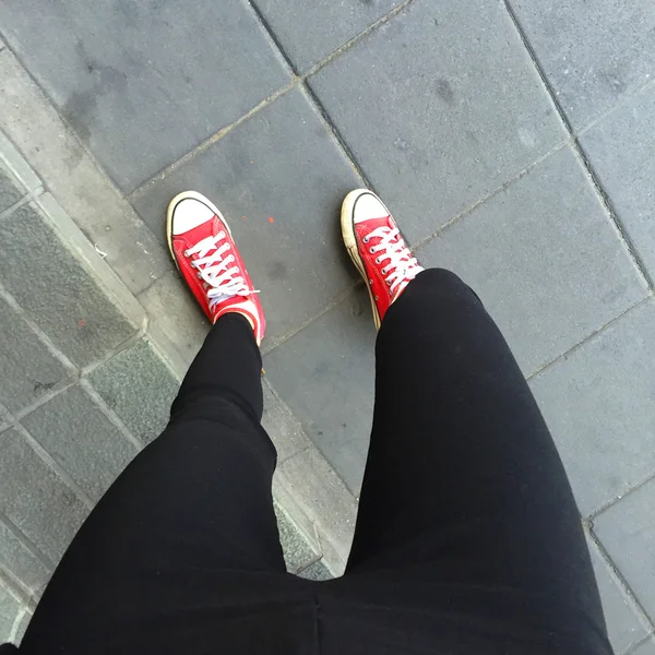 黒のジーンズと床または地面の背景に赤のスニーカーを身に着けている足のクローズ アップ — ストック写真