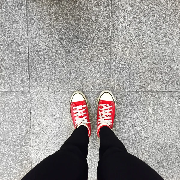 Rote Turnschuhe auf Mädchenbeinen auf dem Boden Hintergrund — Stockfoto