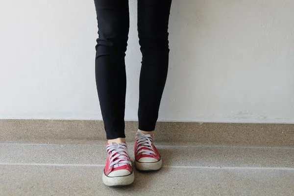 Red sneakers on girl legs on ground background — Stock Photo, Image