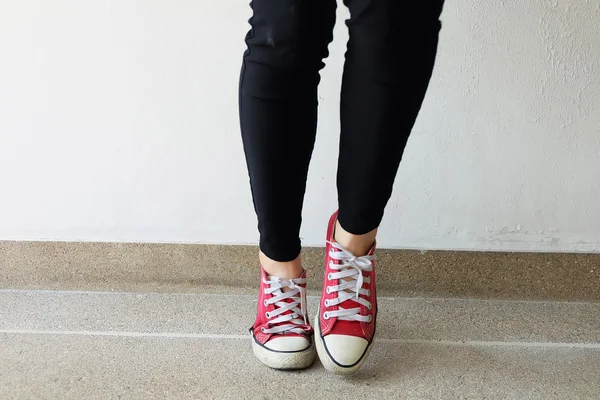 Red sneakers on girl legs on ground background — Stock Photo, Image