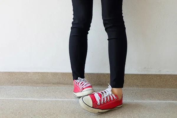 Rode sneakers op meisje benen op de grond achtergrond — Stockfoto