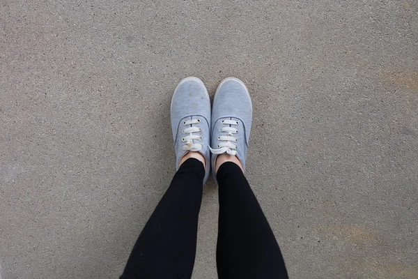 Ung mode kvinnans ben i jeans och sneakers på golvet — Stockfoto