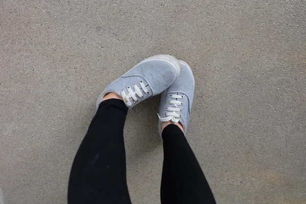 Ung mode kvinnans ben i jeans och sneakers på golvet — Stockfoto