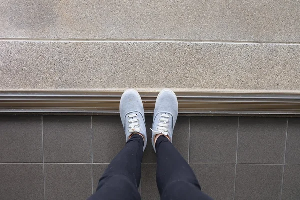 Genç kadının bacakları kot pantolon ve spor ayakkabı katta moda — Stok fotoğraf