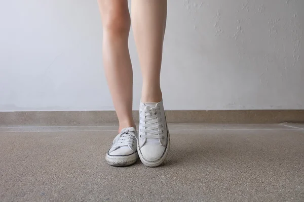 Zapatillas blancas en las piernas de la muchacha en el suelo —  Fotos de Stock