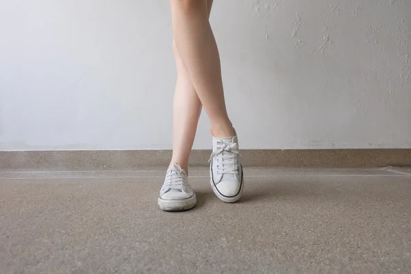 Weiße Turnschuhe auf Mädchenbeinen auf dem Boden — Stockfoto