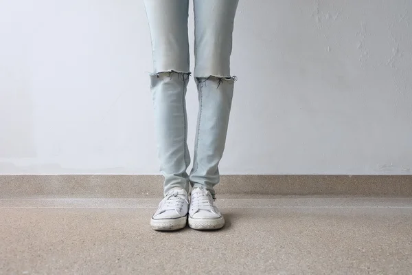 Junge Modefrau in blauen Jeans und weißen Turnschuhen auf dem Boden — Stockfoto