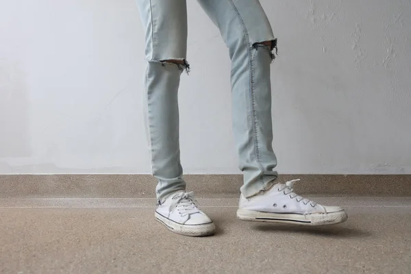 Молода мода жінка ноги в синіх джинсах і білі кросівки на підлозі — стокове фото