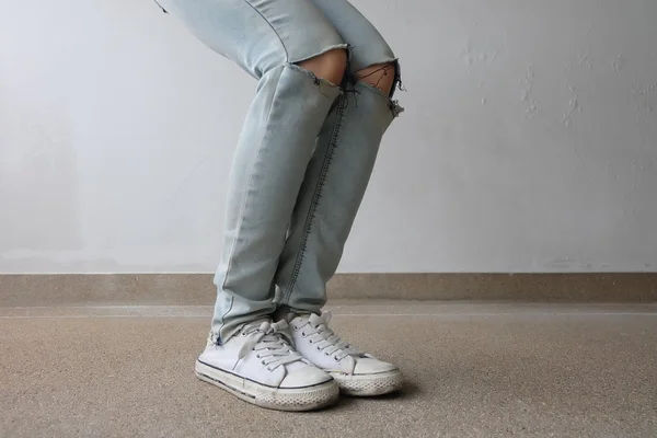 Jonge mode vrouw benen in blauwe jeans en witte sneakers op de vloer — Stockfoto