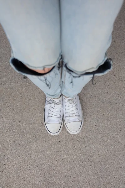 Mladá módní žena nohy v modrých džínách a bílých teniskách na podlaze — Stock fotografie