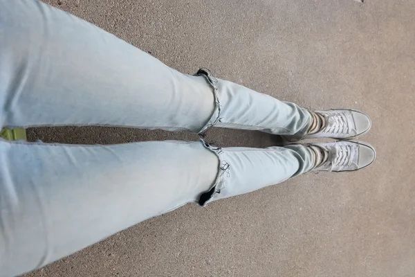 Τα πόδια της νεαρής γυναίκας της μόδας σε μπλε τζιν και λευκά αθλητικά παπούτσια στο πάτωμα — Φωτογραφία Αρχείου