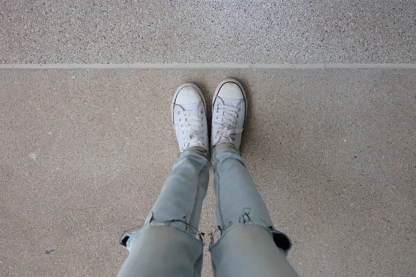 Ноги молодой женщины моды в синих джинсах и белых кроссовках на полу — стоковое фото
