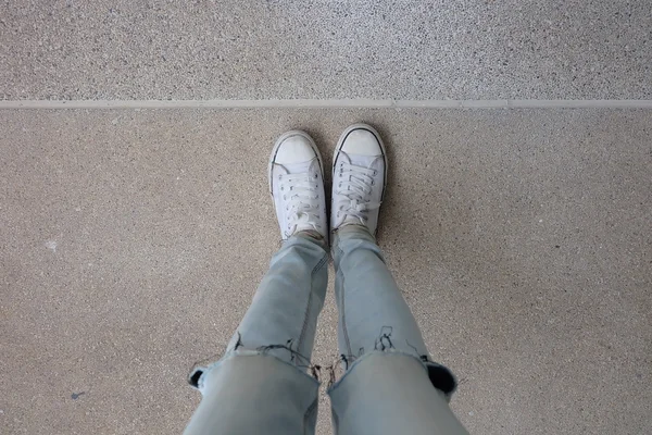 Junge Modefrau in blauen Jeans und weißen Turnschuhen auf dem Boden — Stockfoto