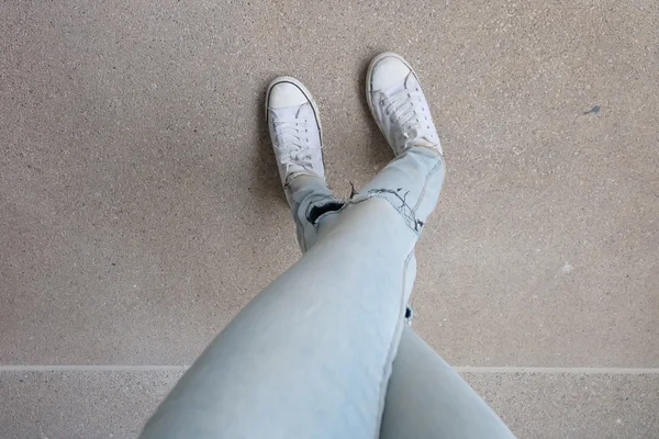 Fiatal Fashion Női lábak Blue Jeans és a fehér cipők a padlón — Stock Fotó