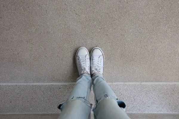 stock image Young Fashion Woman's Legs in Blue Jeans and White Sneakers on Floor 