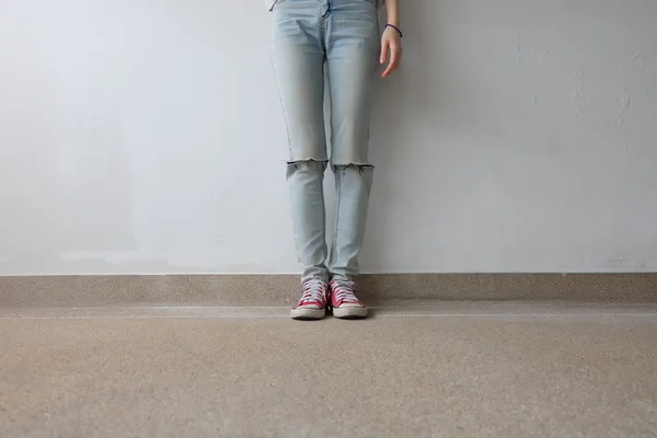 蓝色牛仔裤中的年轻时尚女性腿和地板上的红色运动鞋 — 图库照片