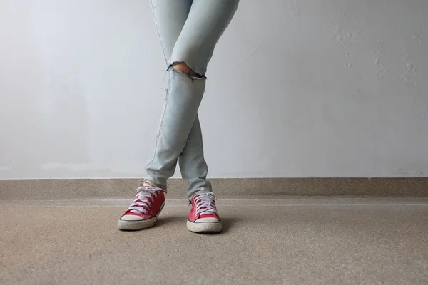 Młoda Moda Woman nogi w niebieskie dżinsy i czerwone sneakers na podłodze — Zdjęcie stockowe