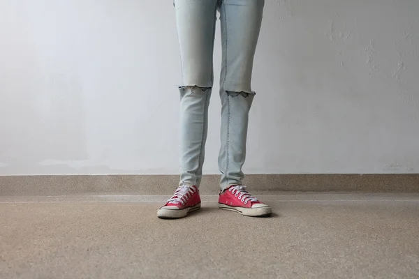 Piernas de mujer de moda joven en pantalones vaqueros azules y zapatillas rojas en el piso —  Fotos de Stock