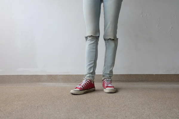 Piernas de mujer de moda joven en pantalones vaqueros azules y zapatillas rojas en el piso —  Fotos de Stock