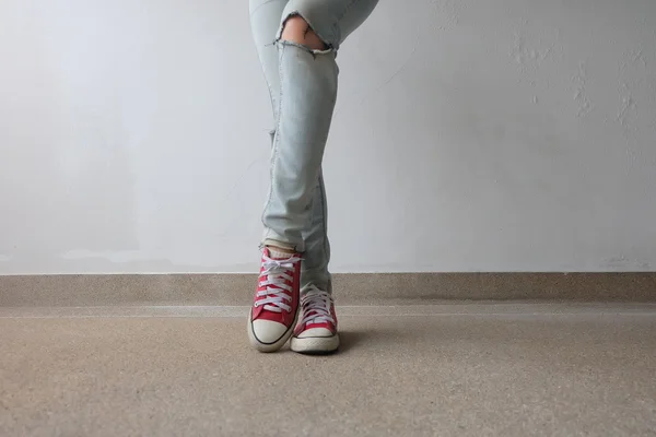 Jonge mode vrouw benen in blauwe jeans en rode sneakers op de vloer — Stockfoto