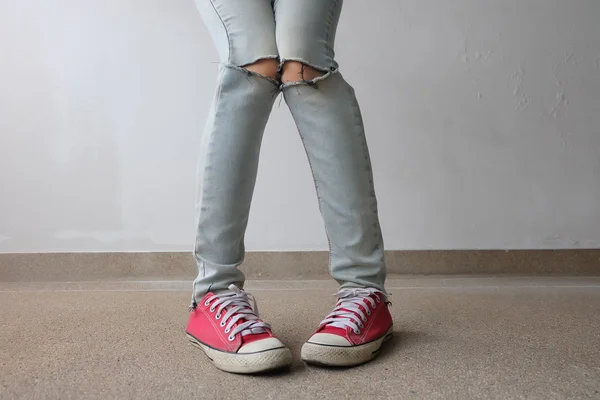 Pernas de mulher de moda jovem em calças de ganga azuis e tênis vermelhos no chão — Fotografia de Stock