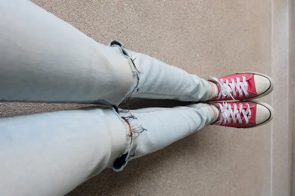 Junge Modefrau in blauen Jeans und roten Turnschuhen auf dem Boden — Stockfoto