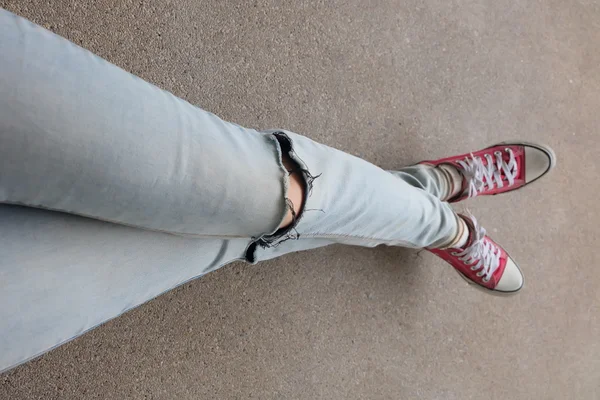 Pernas de mulher de moda jovem em calças de ganga azuis e tênis vermelhos no chão — Fotografia de Stock