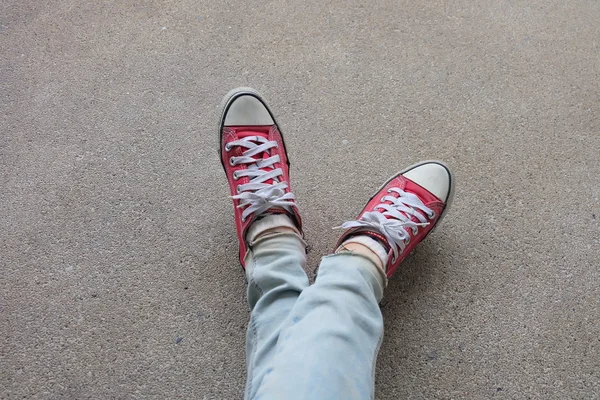 Mladá módní žena nohy v modrých džínách a červených teniskách na podlaze — Stock fotografie
