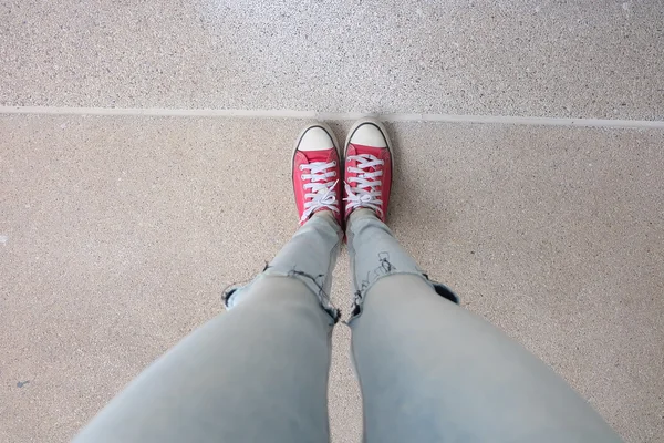 Mladá módní žena nohy v modrých džínách a červených teniskách na podlaze — Stock fotografie