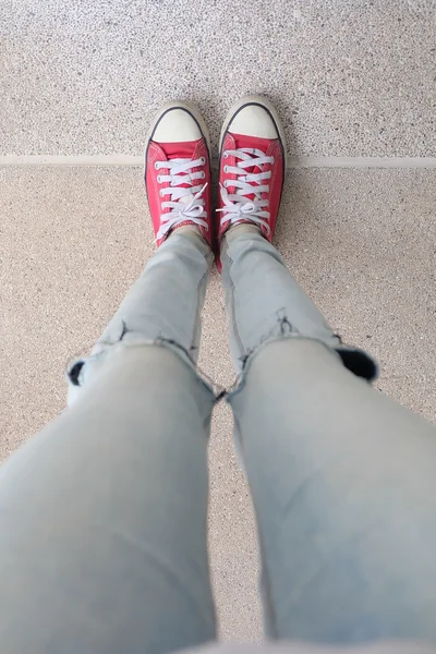 Ноги девушки в синих джинсах и красных кроссовках на полу — стоковое фото