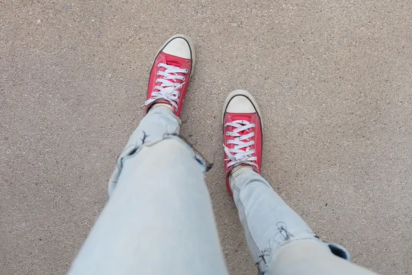 Ноги девушки в синих джинсах и красных кроссовках на полу — стоковое фото