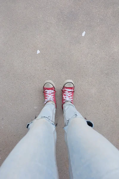 蓝色牛仔裤中的年轻时尚女性腿和地板上的红色运动鞋 — 图库照片