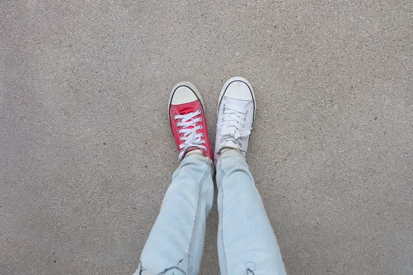 蓝色牛仔裤和白色的年轻时尚女人的腿, 地板上的红色运动鞋 — 图库照片