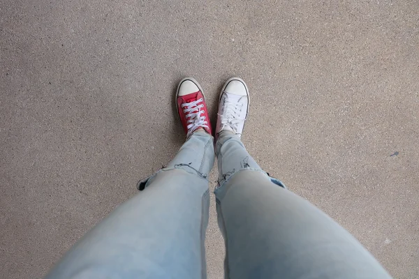 Jonge mode vrouw benen in blauwe jeans en wit, rode sneakers op de vloer — Stockfoto
