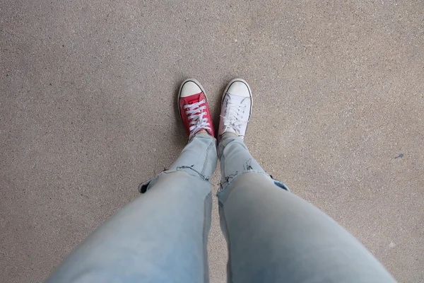 Unga mode kvinnans ben i blå jeans och vit, röda sneakers på golvet — Stockfoto