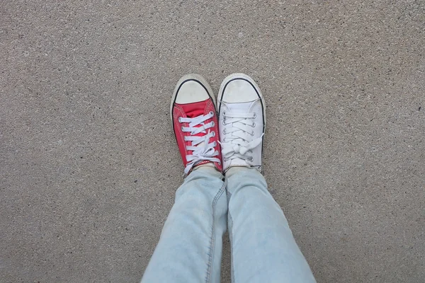 Gambe da donna di moda giovane in blue jeans e bianco, scarpe da ginnastica rosse sul pavimento — Foto Stock