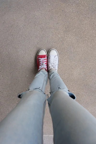 Junge Modefrau in blauen Jeans und weißen, roten Turnschuhen auf dem Boden — Stockfoto