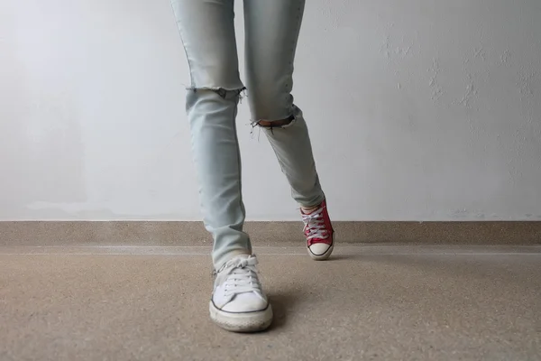 Unga mode kvinnans ben i blå jeans och vit, röda sneakers på golvet — Stockfoto