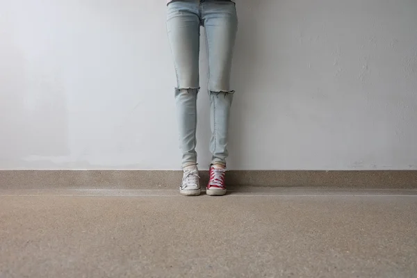 Τα πόδια της νεαρής γυναίκας της μόδας σε μπλε τζιν και λευκό, κόκκινα αθλητικά παπούτσια στο πάτωμα — Φωτογραφία Αρχείου