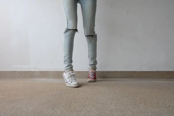 若いファッションの女性の足は、ブルージーンズと白、床に赤いスニーカー — ストック写真