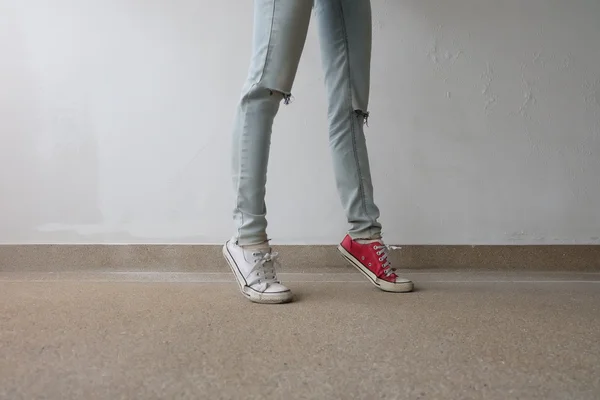 Young Fashion Woman 's Legs in Blue Jeans and White, Red Sneakers on Floor — стоковое фото