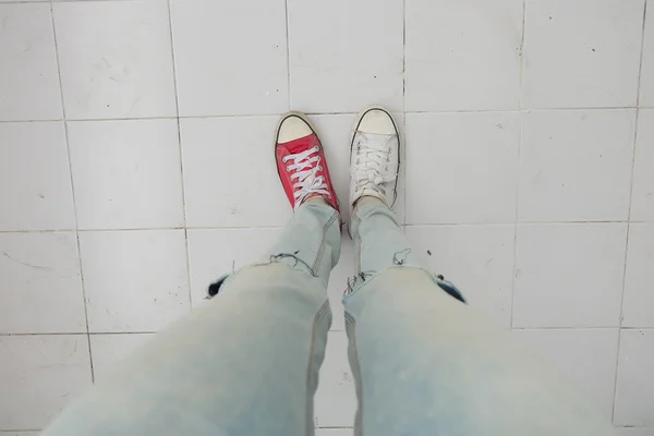 蓝色牛仔裤和白色的年轻时尚女人的腿, 地板上的红色运动鞋 — 图库照片