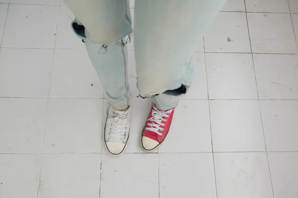 Pernas de mulher de moda jovem em azul jeans e branco, tênis vermelho no chão — Fotografia de Stock