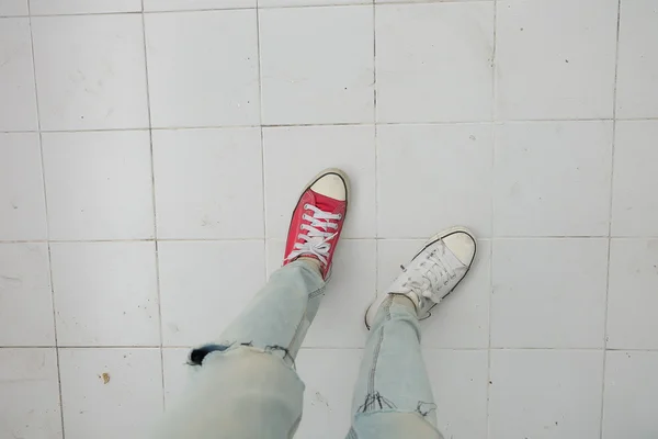 Pernas de mulher de moda jovem em azul jeans e branco, tênis vermelho no chão — Fotografia de Stock
