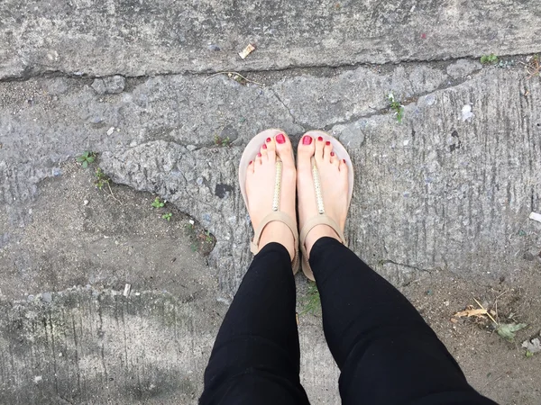 Kvinnliga ben bär skor eller flip-flop utomhus röd spik på golvet bakgrund — Stockfoto