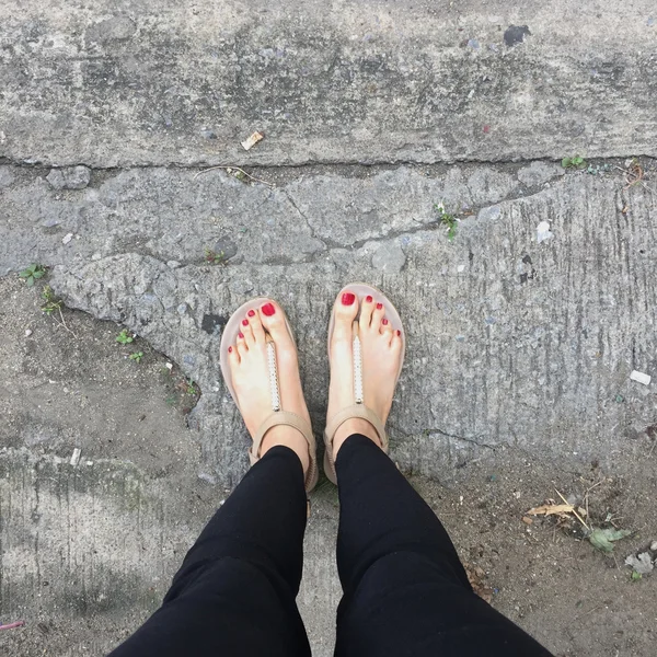 Piernas femeninas que usan zapatos de calzado o chancla al aire libre clavo rojo en el fondo del piso —  Fotos de Stock